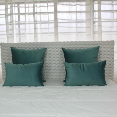 Cabeceira cinza de padrão texturizado com quatro almofadas verdes sobre roupa de cama branca
