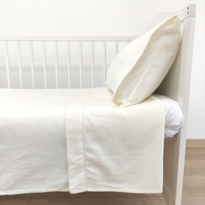 Cama de criança branca com roupa de cama creme e almofada