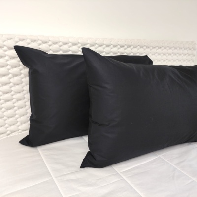 Duas almofadas pretas sobre cama branca com cabeceira texturizada branca.