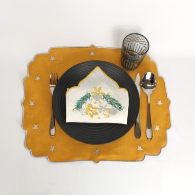 Mesa posta com prato preto, talheres prateados, copo transparente e guardanapo bordado, sobre jogo americano amarelo com estrelas.