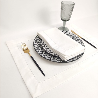 Conjunto de mesa com prato decorado, guardanapo branco, talheres preto e dourado, e copo cinza em relevo
