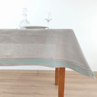 Toalha cinzenta com linhas azuis numa mesa de madeira com prato, copo e garrafa de vidro