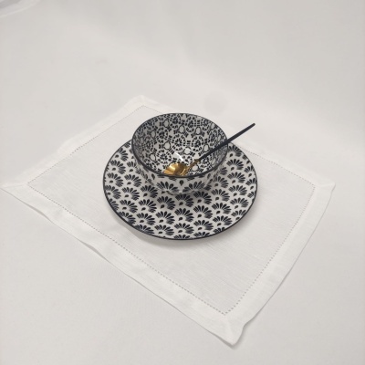 Tigela e prato cerâmicos preto e branco com colher pequena preta e dourada sobre guardanapo branco