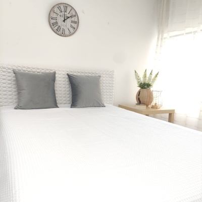 Quarto minimalista com cama branca, almofadas cinzentas e relógio de parede