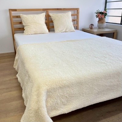 Colcha e almofadas felpudas creme numa cama de madeira em quarto com mesa e flores