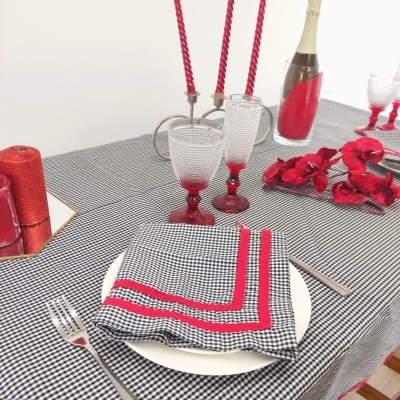 Mesa posta com toalha xadrez, guardanapos, copos, velas e garrafa decorativa vermelha