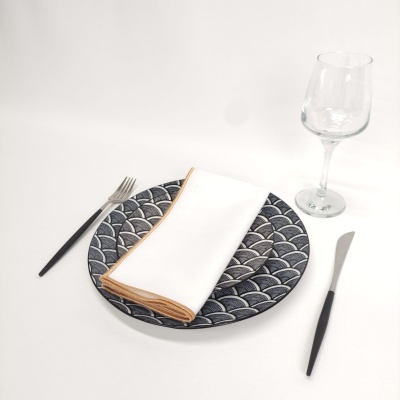 Conjunto de jantar com prato azul com padrão de escamas, guardanapo branco, talheres pretos e copo de vidro