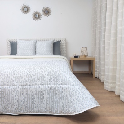 Quarto com cama de casal com edredão branco e almofadas cinzentas, mesa de cabeceira e cortinas claras