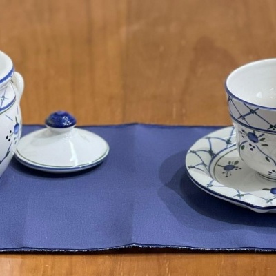 Conjunto de chá porcelana branca com padrão azul sobre base azul numa mesa de madeira