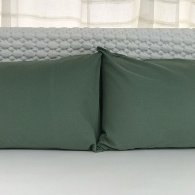 Duas almofadas verdes retangulares sobre cabeceira acolchoada cinza claro