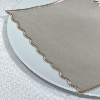 Guardanapo bege com borda ondulada em prato branco sobre toalha branca