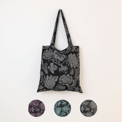 Saco de tecido preto com padrão floral cinzento, pendurado numa parede branca