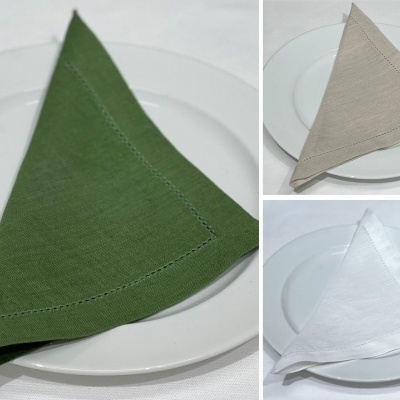 Conjunto de guardanapos triangulares em tecido verde, bege e branco sobre pratos brancos