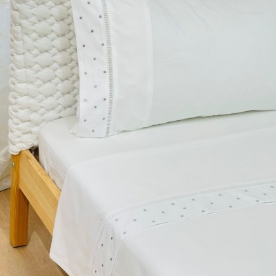 Lençol branco com padrão cinza e fronha combinando numa cama com cabeceira acolchoada branca