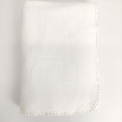 Manta branca com textura quadriculada e borda com pompons pequenos