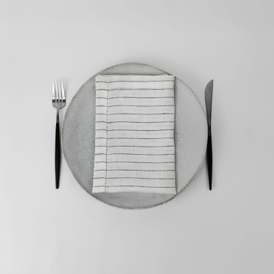 Conjunto de jantar com prato cinza, guardanapo branco com riscas pretas, garfo e faca