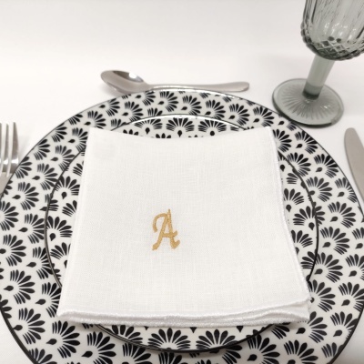 Prato decorado com padrão preto e branco, guardanapo branco com letra A dourada, talheres e copo verde.