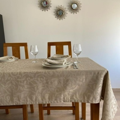 Mesa de jantar com toalha bege floral, pratos, copos, talheres e três cadeiras de madeira