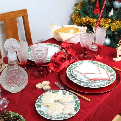 Mesa de jantar de Natal decorada com pratos brancos com borda verde e vermelha e copos de vidro texturizados