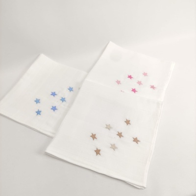 Três panos brancos com estrelas bordadas em azul, rosa e castanho claro