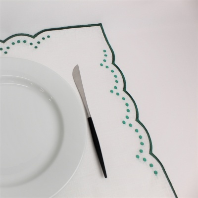 Guardanapo branco com bordado verde, prato branco e faca com cabo preto numa mesa branca