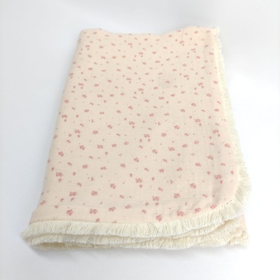 Manta creme com padrão floral rosa e franjas.
