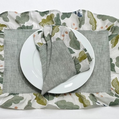 Conjunto de jantar com prato branco, individual e guardanapo com padrão de folhas verdes e amarelas.