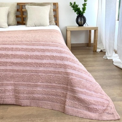 Cama com manta rosa e almofadas brancas num quarto com mesa de apoio e vaso preto com planta