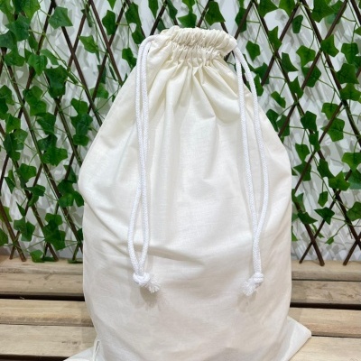 Saco branco de tecido com cordões brancos sobre madeira com fundo de folhagem verde