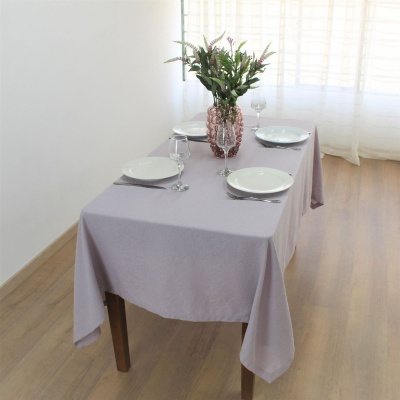 Mesa posta com toalha lilás, pratos, copos e vaso com flores verdes no centro