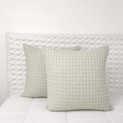 Almofadas texturizadas bege claro sobre colchão branco com cabeceira acolchoada