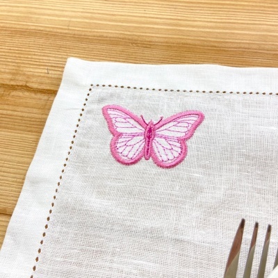 Guardanapo branco com bordado de borboleta cor-de-rosa e garfo sobre mesa de madeira
