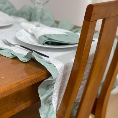 Toalha branca com bordas verdes onduladas numa mesa de madeira com utensílios de jantar