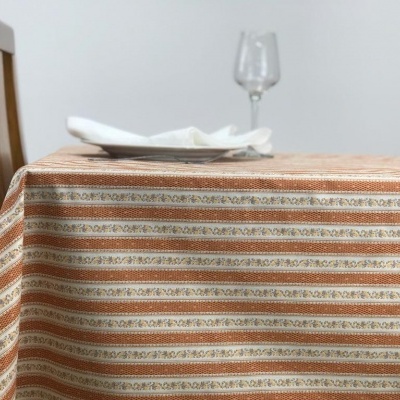 Toalha de mesa listrada em tons castanhos, com copo de vidro, prato branco e guardanapo sobre uma mesa com cadeira de madeira