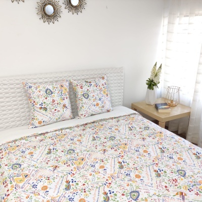 Colcha e almofadas estampadas multicoloridas em cama, mesa de cabeceira com jarro de flores e espelhos redondos na parede