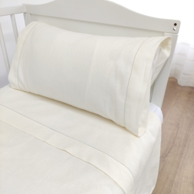 Almofada creme com lençol da mesma cor em cama branca de madeira