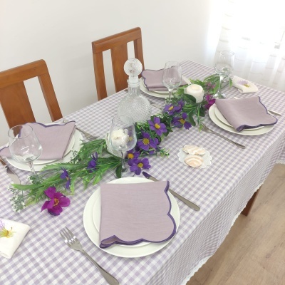 Mesa posta com toalha xadrez, pratos brancos, guardanapos lilás, talheres metálicos, taças de vidro, decantador e flores decorativas