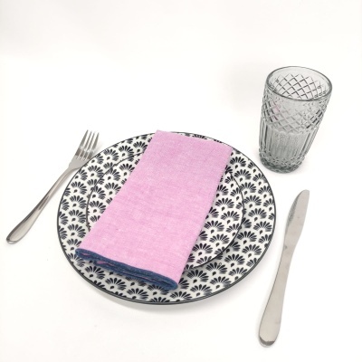 Conjunto de jantar com prato padrão preto em cerâmica, guardanapo rosa, talheres de metal e copo de vidro texturizado