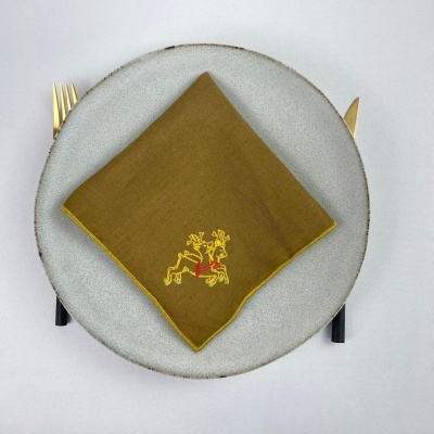 Guardanapo verde-oliva com bordado sobre prato cinza e talheres dourados com cabos pretos