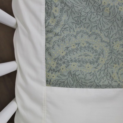 Almofada branca com padrão floral verde e amarelo sobre cadeira branca de madeira