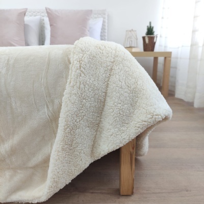 Cobertor de pele de carneiro creme e tecido bege numa cama em quarto com decoração clara