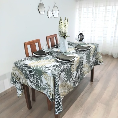 Mesa de madeira com toalha estampada de folhas verdes e bege e decoração simples.