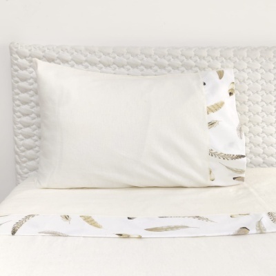 Conjunto de cama branco com fronhas decoradas e faixa com padrão de penas douradas