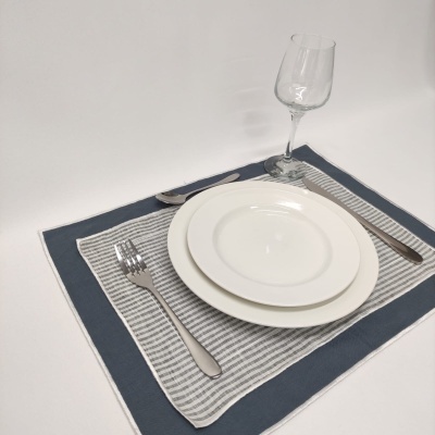 Conjunto de jantar com pratos brancos, talheres de metal e copo sobre toalha azul com toalha riscada