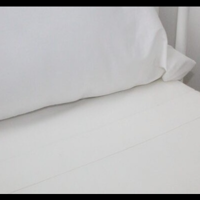 Lençol e fronha brancos numa cama com cabeceira branca.