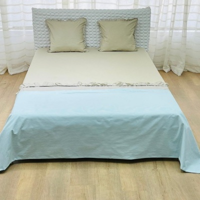 Cama com cabeceira de tecido branco e roupa de cama bege e azul