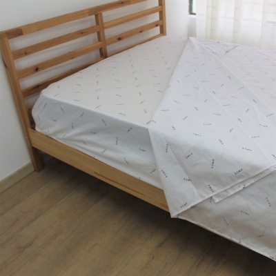 Cama de madeira clara com lençóis brancos estampados com padrão de texto em ambiente iluminado