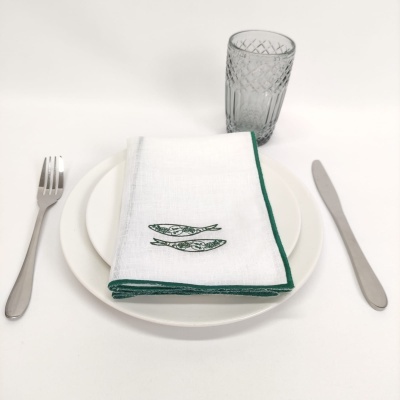 Conjunto de prato branco com faca, garfo, copo cinza e guardanapo branco com bordas verdes e peixes verdes