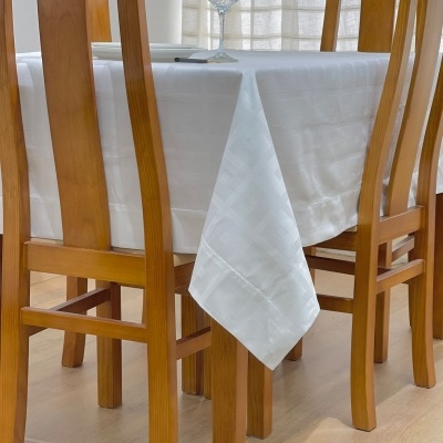 Mesa de madeira clara com toalha branca e cadeiras de madeira