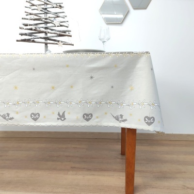 Toalha de mesa branca com padrões de corações, pássaros e estrelas em cinza e dourado sobre mesa de madeira